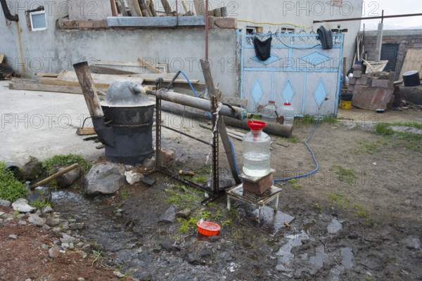 Self-built distillation plant in front of a rural farm with various materials, production of