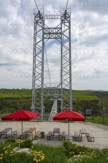 A tall metal structure with seating and red umbrellas in the foreground of nature, Diamond Bridge,