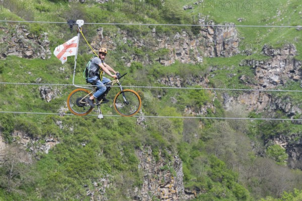 Man on a bicycle balancing at lofty heights above a green valley, Dashbashi Gorge, Khrami River,