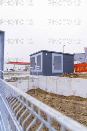 Shed on a fenced area with earthworks in the foreground, parking garage construction with charging