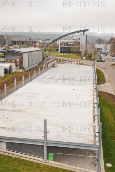 Aerial view of an empty parking lot with surrounding buildings and fences, parking garage