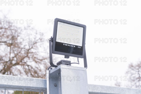 A Trilux LED lamp is mounted on a metal post, with cloudy sky, parking garage construction with