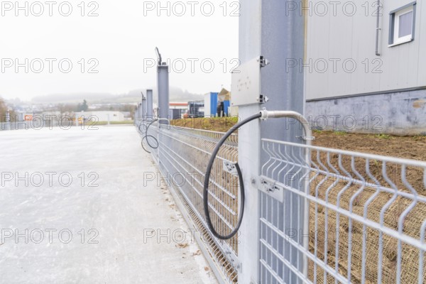 A cable is attached to a fence along a concrete surface. Industrial environment in the background,