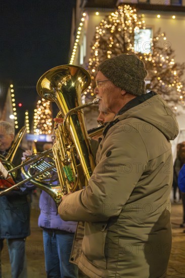 Tuba player in winter clothes on a street decorated with lights, Weihnachtsmark Nagold,