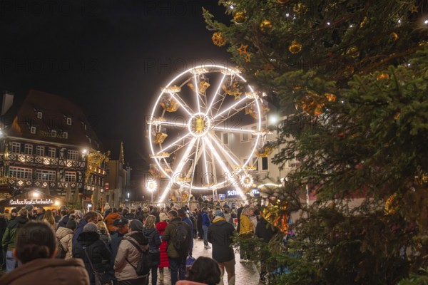 Illuminated Ferris wheel and half-timbered houses at night on a busy Christmas market,