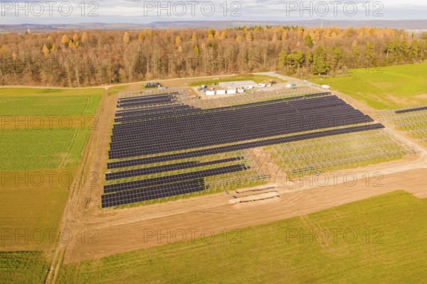 Aerial view of a solar park surrounded by fields and autumn forest, energy revolution, construction