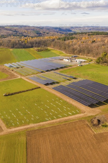 Aerial view of a solar park surrounded by fields and autumn forests, energy revolution,