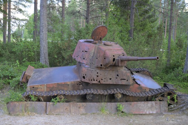 Rusted tank in the forest with visible signs of age and vegetation, museum at the Winter War
