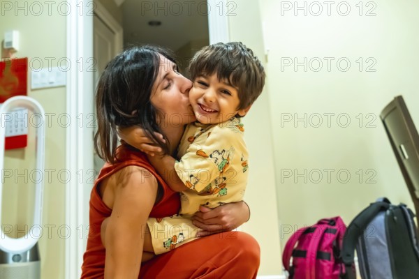 Happy mother kissing her cheerful son on the cheek while holding him in her arms, enjoying a warm