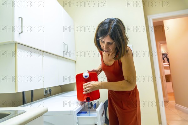 Housewife carefully pouring blue laundry detergent from a red container into the washing machine