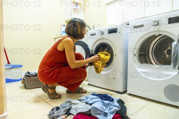 Woman loading clothes into a washing machine in a bright, modern laundry room, engaging in regular
