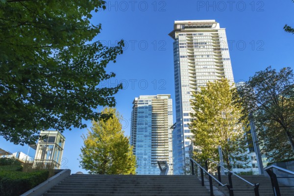 Modern skyscrapers rise above green trees in vancouver, british columbia, on a clear sunny day,