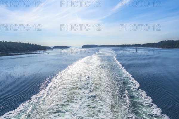 Sparkling ocean water reflects sunlight in the wake of a ferry traveling between islands near