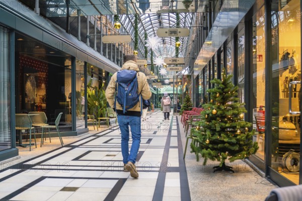 Person walking through a festively decorated shopping center with glass roof, Calwer Passage,