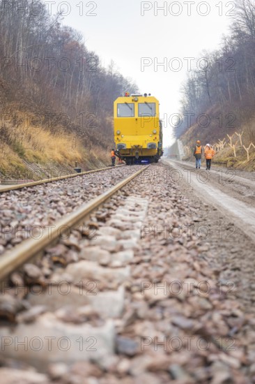 Yellow work train runs on a railroad track with workers on the line, stuffing machine on Hermann,