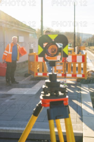 Measuring device on stand in front of worker in safety vest in sunny weather, stuffing machine on