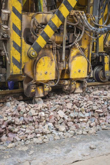 Large construction machine in use. Gravel and yellow-black markings visible, tamping machine on
