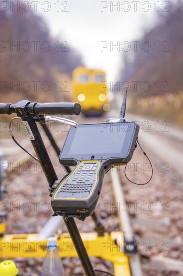 A technical device with a screen in front of a yellow vehicle on the rails, tamping machine on