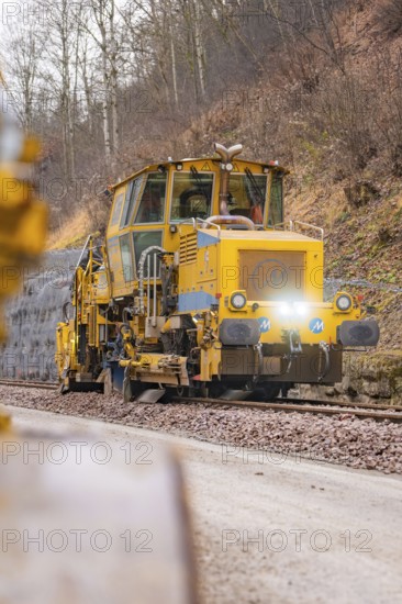 Yellow track construction equipment on tracks with wooded track under construction, tamping machine