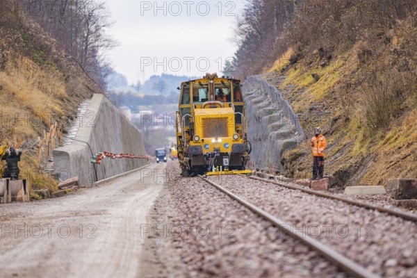 Rail construction machine in the landscape, workers seen along the tracks, tamping machine on