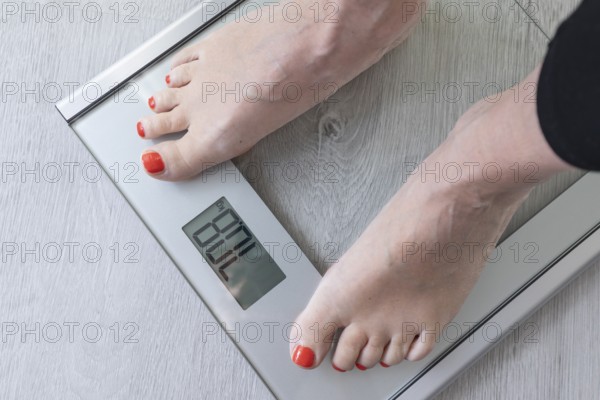 Feet of a woman standing on a digital bathroom scale while monitoring her weight. This scene