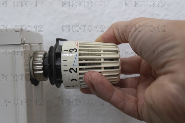 A hand grabs the thermostat head of a radiator to adjust the temperature. This image symbolizes