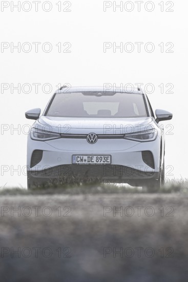 A white car seen from the front in a morning haze in an open landscape, VW ID4 electric car, Deer