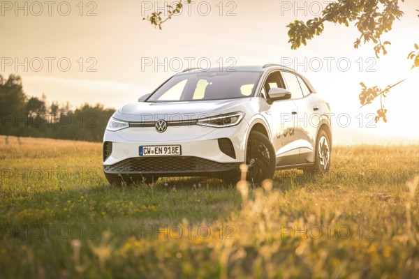 White car standing in a field in warm sunlight at sunset surrounded by grass, VW ID4 electric car,