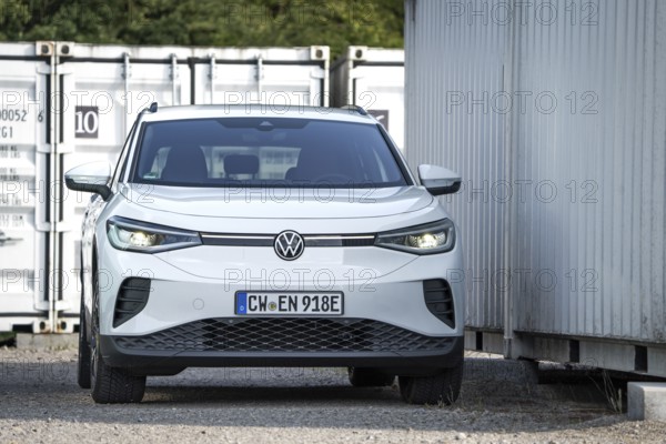 A white car parks between industrial containers and buildings, VW ID4 electric car, Deer