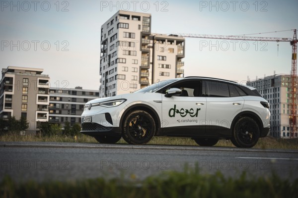 A white car is parked on a street with modern buildings in the background, VW ID4 electric car,