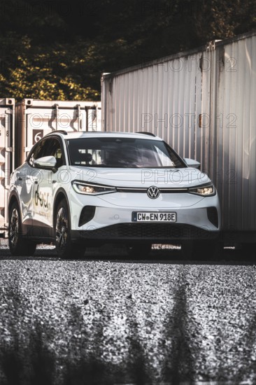 A car on a gravel field next to stacked containers in the shade, VW ID4 electric car, Deer