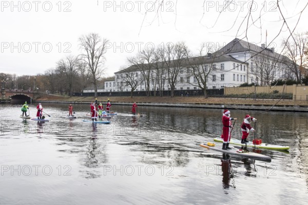 Water sports enthusiasts dressed up as Santa Claus ride SUPs on the Spree in front of Bellevue