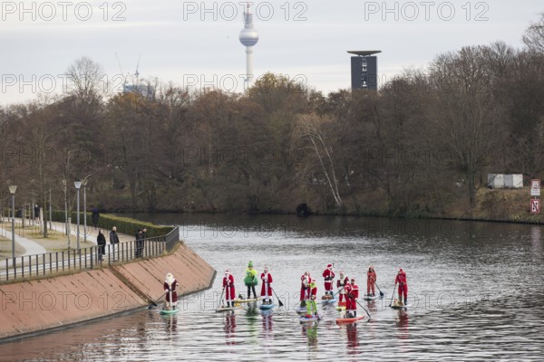 Water sports enthusiasts dressed up as Santa Claus ride SUPs on the Spree am Park at the