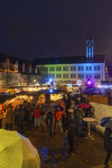 Colourfully lit Christmas market with people and umbrellas in a nighttime urban landscape,
