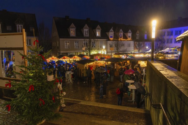 Christmas market at night, lots of visitors with umbrellas, Christmas tree and bright lights,
