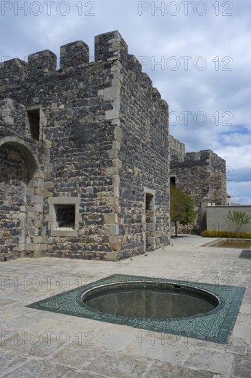 Part of a massive stone castle with battlements and a decorative fountain in the courtyard, Rabati