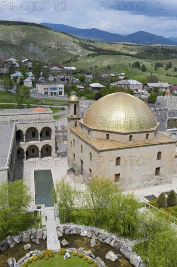 Mosque with golden dome and surrounding garden, nestled in a hilly landscape, Rabati Fortress,
