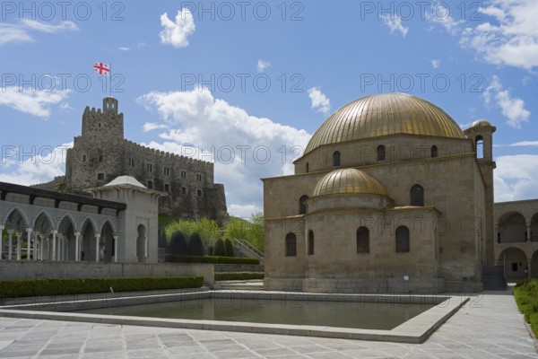 Mosque with golden dome in front of a stone castle with flag under clear sky, Rabati Fortress,
