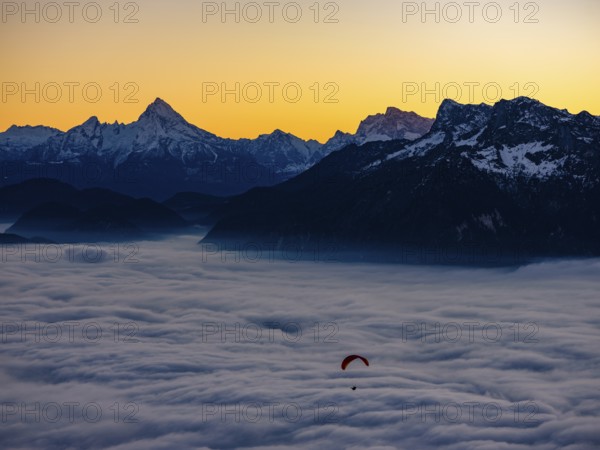 Paragliding flies over a sea of fog, behind Berchtesgaden Alps with Watzmann, Hochkalter and