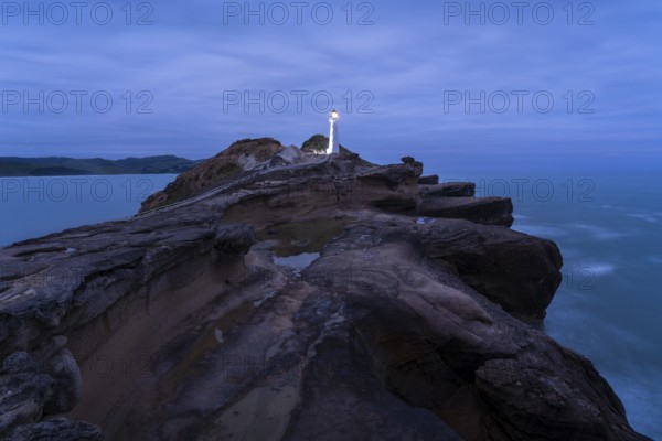 Castlepoint lighthouse on a rock, ocean, evening, blue hour, illuminated, long exposure.