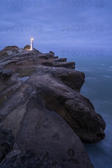 Castlepoint lighthouse on a rock, ocean, evening, blue hour, illuminated, long exposure.