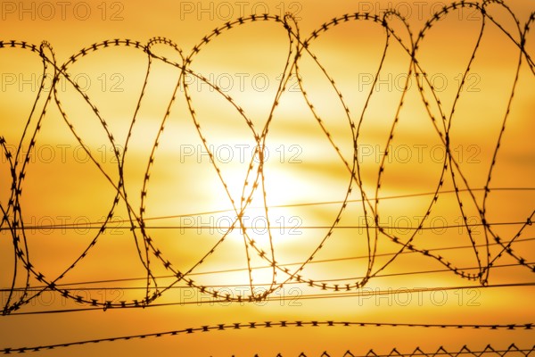 Sun sets behind barbed wire fence, bright orange and yellow tones, Baden-Württemberg, Germany