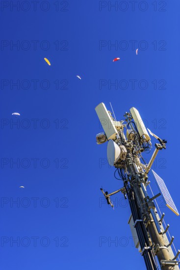 Paragliders with colored paragliders fly over the transmitter and cell phone tower at the summit of