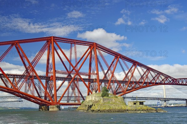 A large, red bridge stretches over water, on which a small island lies, fortification from the