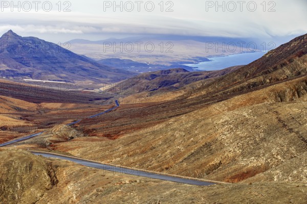 Road leads through the mountainous landscape of Fuerteventura with extensive views over the sea,