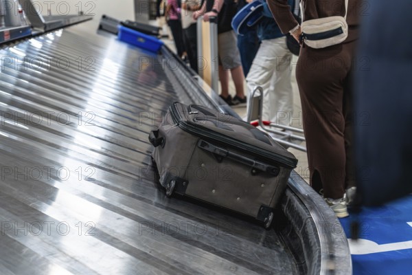 Passengers waiting at the baggage claim carousel in the airport, watching as a suitcase arrives on
