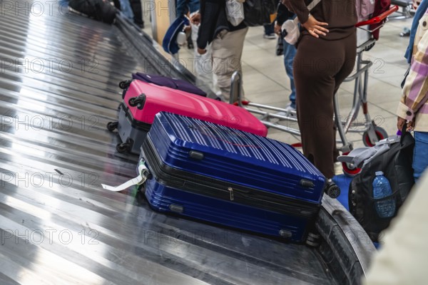 Colorful suitcases resting on an airport baggage claim carousel, while passengers eagerly waiting