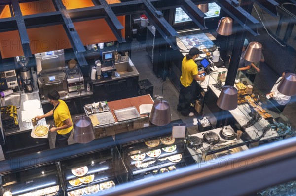 Chefs working in a busy airport restaurant kitchen prepare various dishes, including pizza and