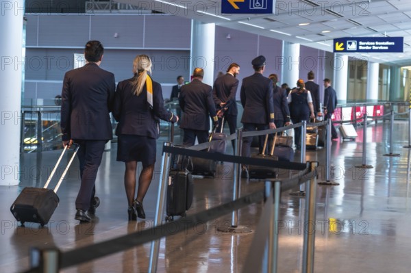 Pilots and flight attendants are walking through a modern airport terminal, pulling rolling