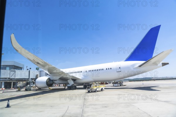 White and blue passenger airplane parked at the airport gate, getting ready for departure under a